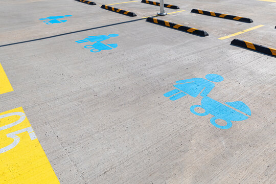 Designated family parking lot spots marked with blue painted symbols of a mother with baby stroller on sunny concrete pavement with yellow lane markings and wheel stops.