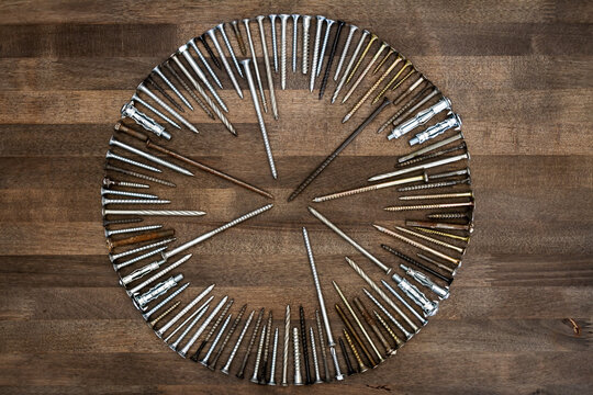 Circle made of various screws and nails on brown wood texture. Industrial flat lay. Carpentry still life.