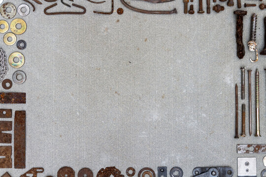 A frame of various old rusty bits and pieces arranged on a concrete surface. Old rusty nuts, bolts, nails and other parts flay lay on gray background.