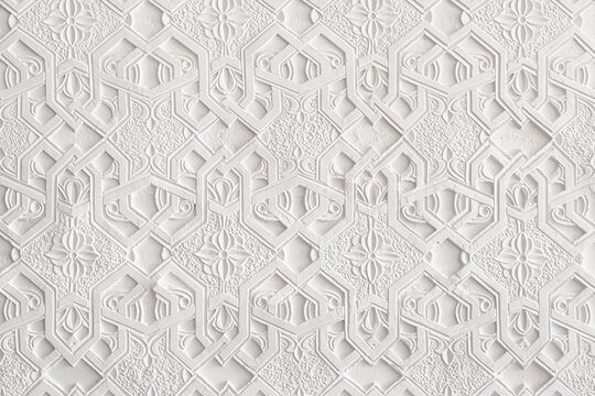 White carved plaster wall with intricate geometric and floral Islamic patterns inside a historic madrasah in Khiva, Uzbekistan. Ideal for backgrounds, textures, and architectural heritage projects.