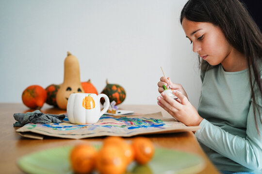 Female kid painting a pumpkin on a cup for an halloween party fest - Holidays and art concept - Main focus on face
