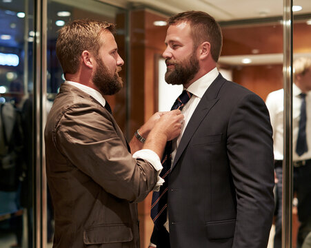 Friend helping groom or businessman adjust his tie before formal event in boutique