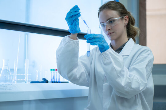 Female scientist examining laboratory tubes working inside a laboratory safety cabinet while conducting sample analysis