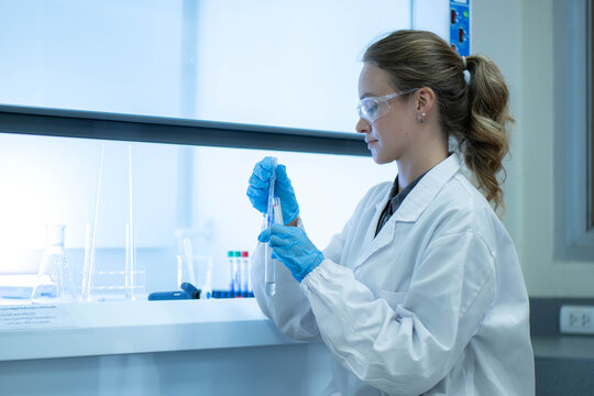 Female scientist examining laboratory tubes working inside a laboratory safety cabinet while conducting sample analysis