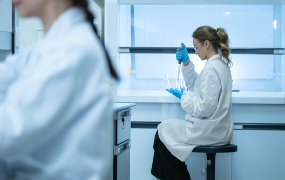 Female scientist examining laboratory tubes working inside a laboratory safety cabinet while conducting sample analysis