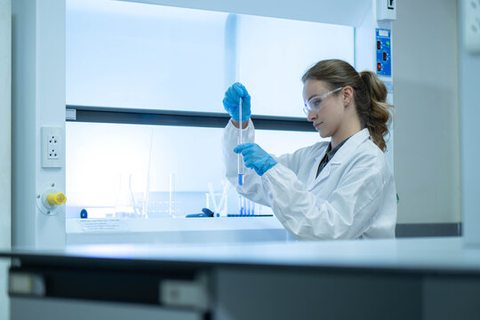 Female scientist examining laboratory tubes working inside a laboratory safety cabinet while conducting sample analysis