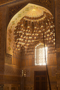 Golden muqarnas vault inside Gur-e-Amir mausoleum in Samarkand with sunlight streaming through a lattice window. Intricate gilded interior ideal for travel publications and cultural heritage projects.