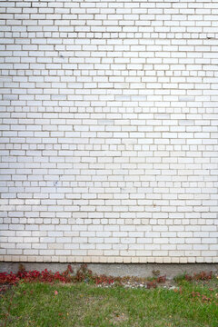 Old cracked white brick wall with green grass. Architectural detail background.