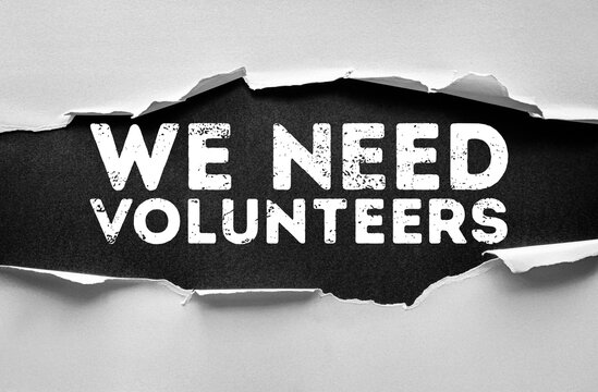Torn paper reveals the bold grunge words WE NEED VOLUNTEERS underneath, symbolizing community help, charity, and social awareness breaking through a surface with distressed typography