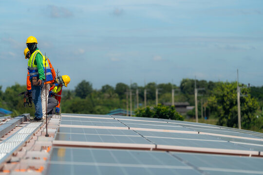 Seen from behind, a solar technician makes his way along the ridge walkway, a lightning rod rising at the end of the walkway - everyday working life on a commercial solar installation.