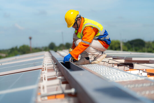 Detail of an installer's hand and drill at a panel clamp on the array, sunlight glancing off the polycrystalline cells - skilled trade work driving the renewable energy transition.