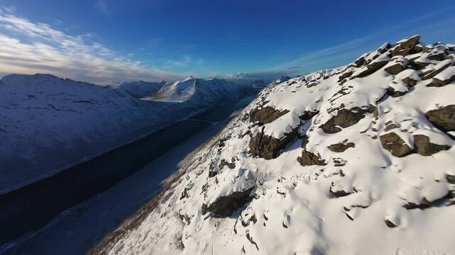 FPV Drone Flying Along Rocky Snow-Covered Mountain Ridge with Dramatic Peaks in Northern Norway