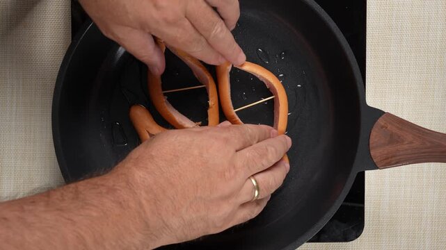 Toothpicks hold two sausages sliced open into boat shapes inside an oiled frying pan. This close-up captures the prep step for a creative sausage and egg recipe.