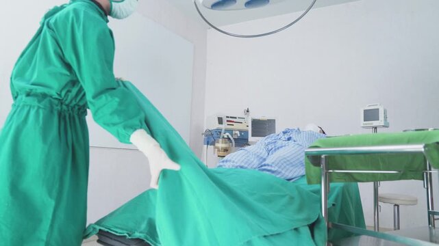 A medical worker covering a patient with a green surgical sheet on an operating table.