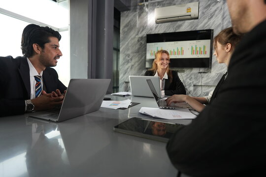 Keyboard clicks from the young teammate as the manager gestures over his laptop, the blonde colleague smiling mid laugh in the bright office in a bright modern coworking office.