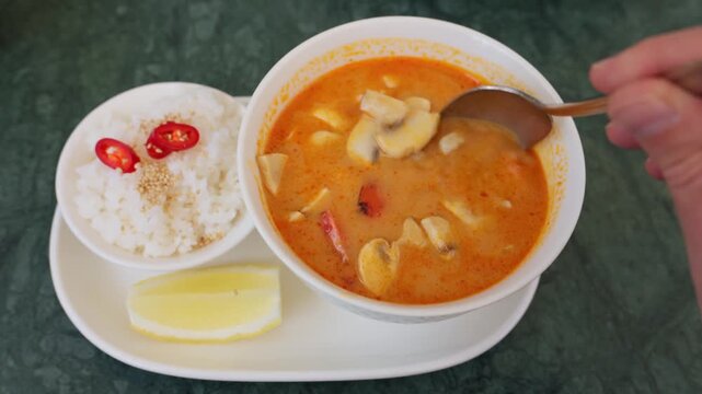 Stirring tom yum soup with shrimp and mushrooms in bowl on table.