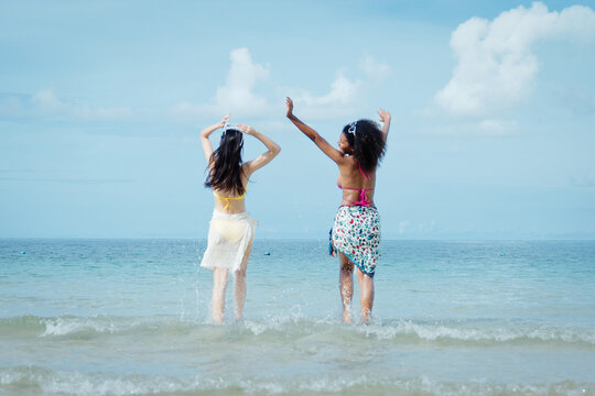 Two girls stand in shallow ocean water, arms raised