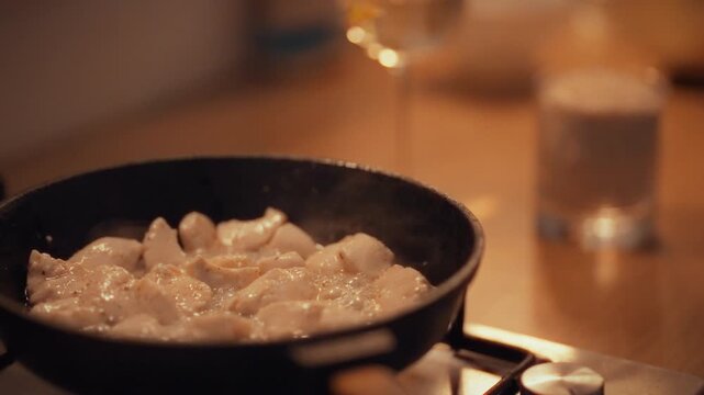 Chef stews chicken pieces in hot frying pan on gas stove, capturing sizzling cooking process as the meat turns golden and releases rich aromas. The kitchen fills with warm aroma, showcasing cooking