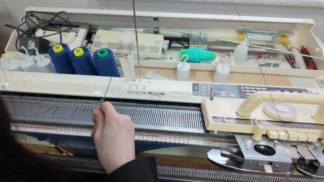 Woman weaving blue thread on vintage industrial knitting machine at craft studio.