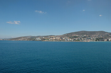 Fototapeta premium A scenic coastal view of the resort town Kusadasi with hotels and buildings on hillsides as seen from the calm blue waters of the Aegean Sea.