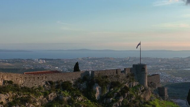 Aerial Drone Shot of a Castle and its Fortifications with a Flag on a Mountain Top during Sunset