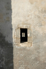 Naklejka premium Close up view of a small rectangular window slot with stone frame on the weathered exterior wall of the historic Church of Panagia Myrtidiotissa on Kythira island