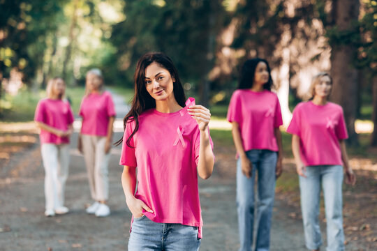 Smiling woman in pink t shirt showing pin ribbon, diverse group of women on background on the street