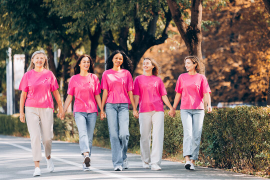 Diverse group of smiling happy women in pink t shirts with ribbon holding hands walking