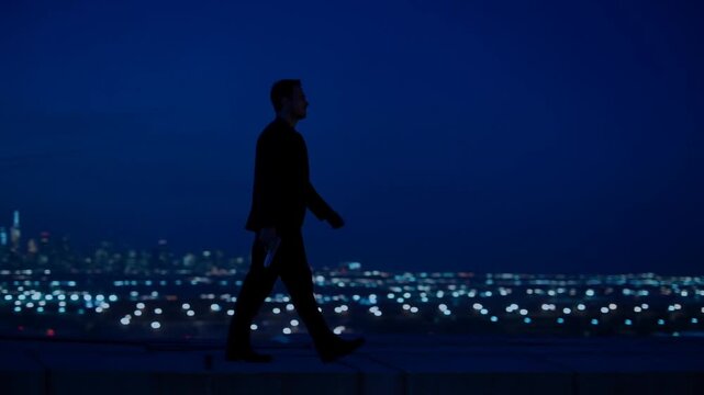Tracking shot man walking along rooftop edge at night with city lights skyline in background, silhouetted profile pacing across ledge