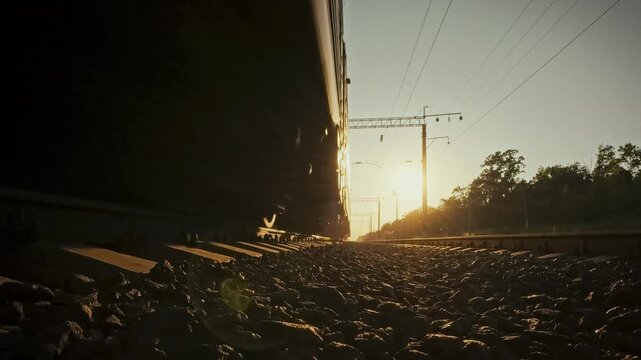 Close-up of the sleeper rails and wheelsets of a passing freight train on a sunny day. The concept of railway infrastructure and track maintenance in field areas