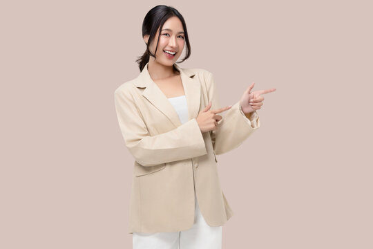 Happy young Asian businesswoman pointing both fingers to copy space with a cheerful smile, studio portrait on beige background.