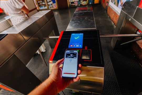 Hand holding smartphone with digital ticket at subway turnstile in Milan, automated fare collection system visible in the background