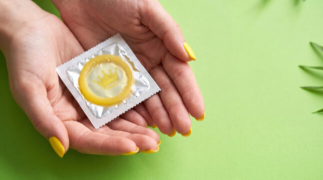 Hands holding a foil-packaged condom on a vibrant green background, promoting safe sex, contraception, and reproductive health awareness.