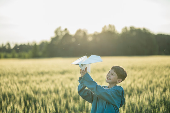 Happy boy launches a paper airplane in a summer field