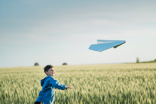 Happy boy throws a paper airplane in a green summer field
