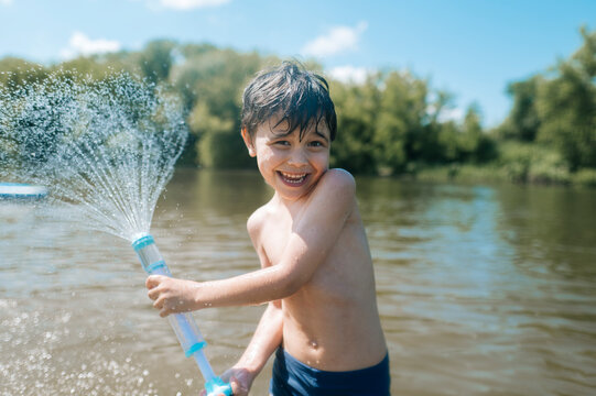 Smiling boy plays with a water toy in the river during summer