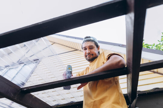 A man repairs a wooden roof with a drill outside the house