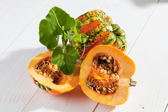Sliced and whole multicoloured squash (Cucurbita maxima) on white wooden table, studio shot