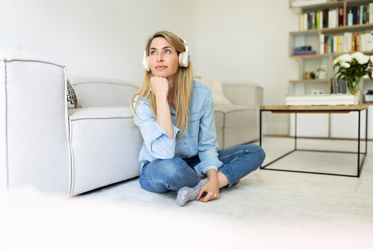 Thoughtful woman listens to music on the living room floor