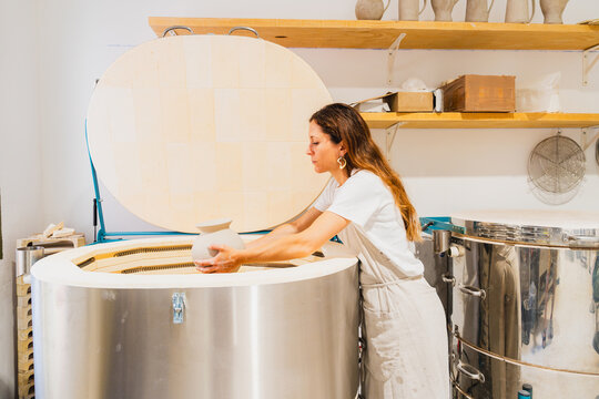 Female potter placing handmade ceramic vase into a kiln