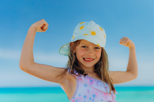 Smiling girl flexes muscle on the beach during summer vacation