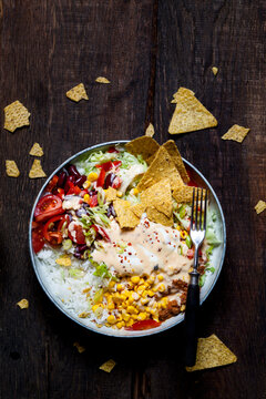 Taco salad bowl with rice, corn, chili con carne, kidney beans, iceberg lettuce, sour cream, nacho chips, tomatoes