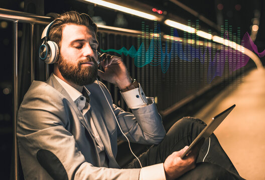 Young man with tablet and headphones sitting on bridge at night