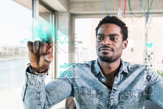 Casual businessman touching glass pane with data in office