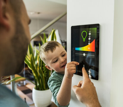 Father and son control smarthome lighting on wall tablet at home