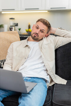 Young man at home works on laptop feels tired and demotivated and takes deep sigh during hard task. Caucasian guy on sofa slumps shoulders shows fatigue stress low energy and tries to focus now again