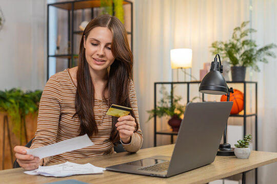 Young woman at home enters credit card number on laptop pays bills checks totals and confirms payment. Caucasian girl at desk reviews page adds cvv presses pay button sees receipt and saves file copy