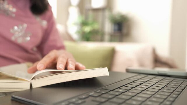 Woman studying and working from home, reading a book while using laptop for online learning, training, career development, professional growth, skills, education and modern digital work.