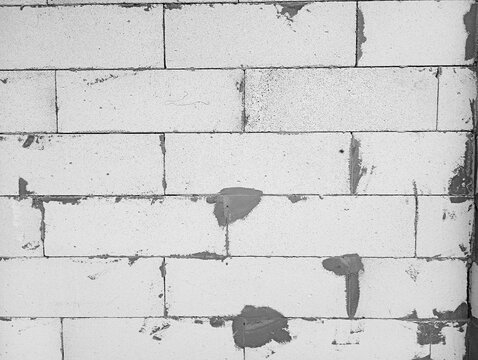 Texture of a raw lightweight concrete block wall with rough grey mortar joints and cement smudges during construction.