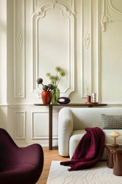 Elegant modern living room interior with white classic wall molding, cozy white sofa, burgundy armchair, and stylish home decor accessories